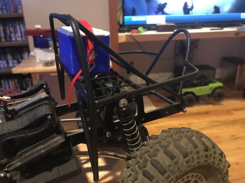 1989 Ford Bronco - Close-up of an RC car chassis a roll cage and a blue box secured with a red strap. Another RC vehicle is visible in the background.