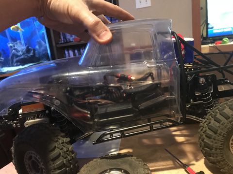 1989 Ford Bronco - A clear plastic RC car body is being held over a black chassis with visible suspension and tires. The interior of the RC car shows wiring a…