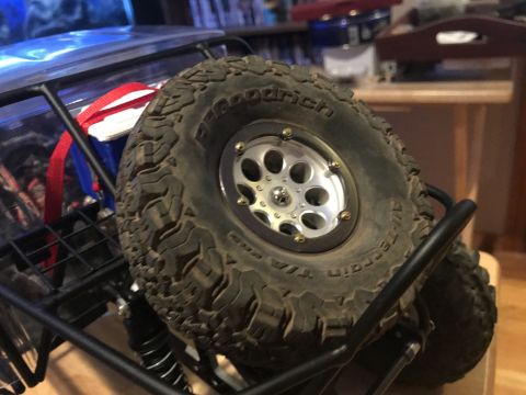 1989 Ford Bronco - A close-up view of a large, knobby off-road tire mounted on a silver multi-spoke wheel, attached to a black roll cage structure. The tire h…