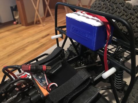 1989 Ford Bronco - A blue and white cooler is strapped to the rear rack of a black RC vehicle. The cooler has the Coleman logo visible and is secured with red…