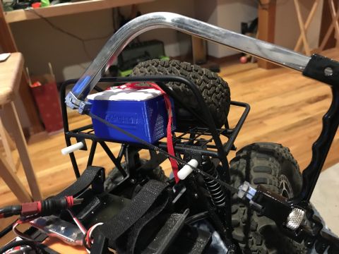 1989 Ford Bronco - A close-up view of the rear of a modified RC vehicle, showing a blue battery box secured with a red strap, a spare tire, and suspension com…
