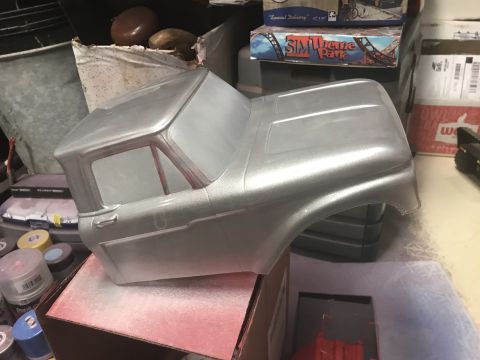 1989 Ford Bronco - A silver, unpainted RC truck body is shown from a 3/4 front angle, resting on a cardboard box with red spray paint residue. Various spray p…