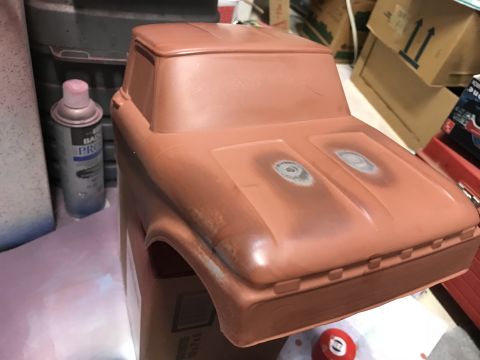 1989 Ford Bronco - A plastic model truck body, painted a reddish-brown, sits on a surface with a spray can and boxes in the background. The hood shows two cir…