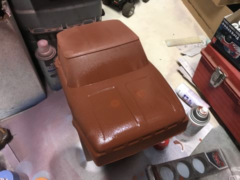 1989 Ford Bronco - A partially painted brown vehicle body, likely for an RC car or model, sits on a work surface next to spray cans and a red toolbox.