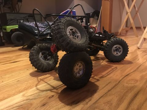 1989 Ford Bronco - RC rock crawlers are displayed indoors on a wood floor, with one vehicle stacked on another.