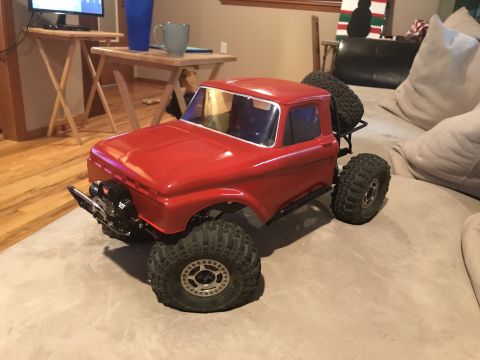 1989 Ford Bronco - A red remote-controlled pickup truck with large off-road tires is parked on a beige couch. The truck has a winch mounted on the front bumpe…