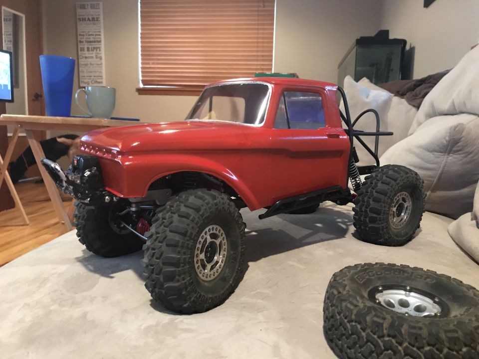 Red RC rock crawler truck with large tires on a couch, with a spare tire in front.