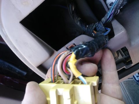1996 Ford Bronco - A hand is holding a yellow electrical connector with multiple colored wires attached, connected to a vehicle's dashboard wiring harness.