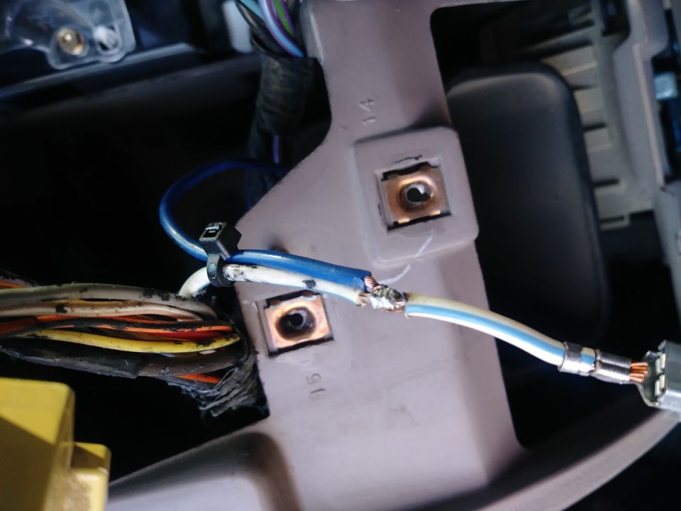 Close-up of spliced blue and white wires connected to a wire bundle, secured by a zip tie to a gray bracket.