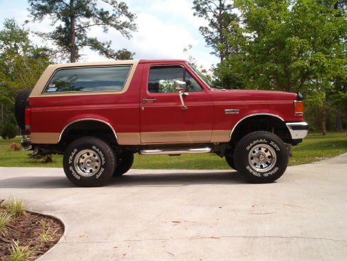Side profile of two-tone red and tan lifted Ford Bronco on a driveway