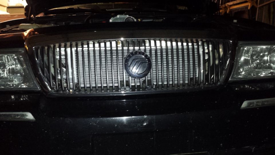 Black sedan front grille with chrome vertical bars and emblem, headlights flanking
