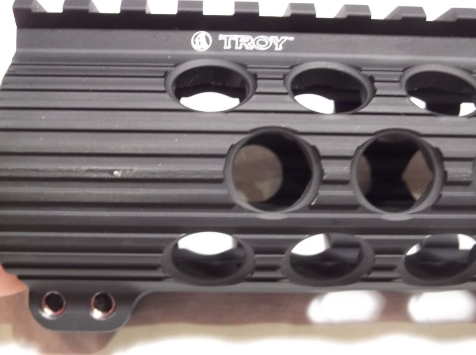 Black Troy Industries rifle handguard with slots and top rails, showing the Troy logo.