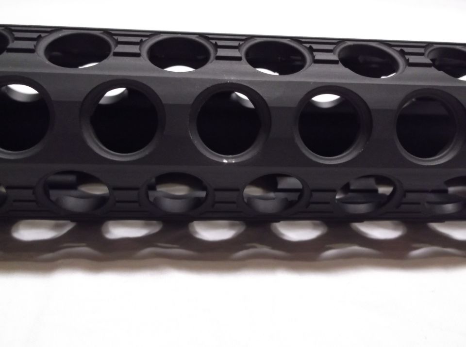 Black firearm handguard with circular cutouts and shadows.