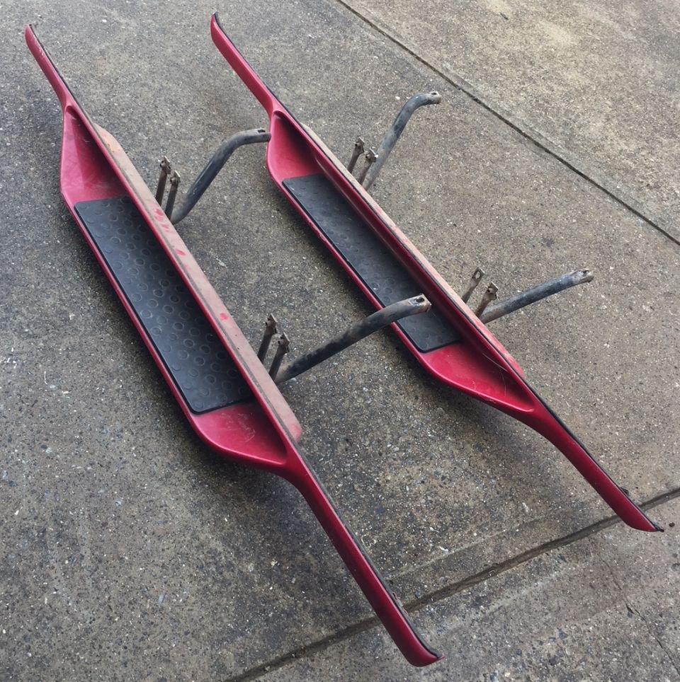 Red aftermarket running boards with black step pads on concrete