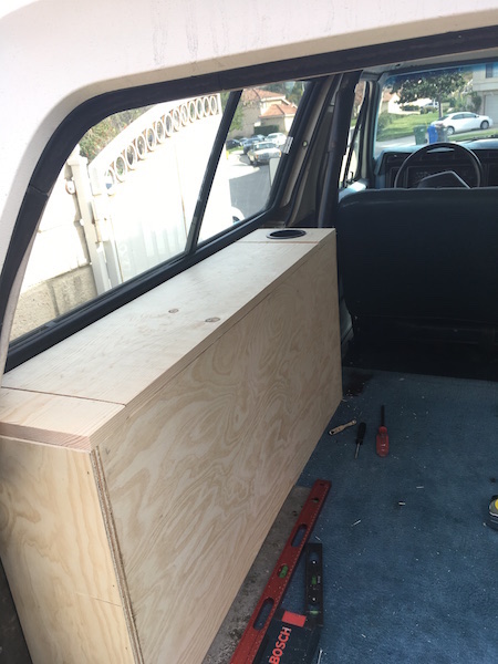 1981 Ford Bronco - A custom wooden storage box is installed in the rear cargo area of an SUV, next to the window. Tools and a level are visible on the blue ca…