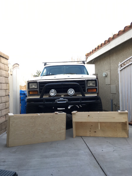 1981 Ford Bronco - A white 1980s Ford Bronco is parked in a driveway with two unfinished wooden storage boxes in front of it. The Bronco has a roof rack and a…