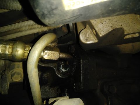 1996 Ford Bronco - Close-up view of a hydraulic line connection on a dark-colored engine block. A metal pipe with a braided hose fitting is secured with a nut…