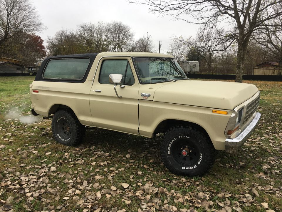 1979 Ford Bronco parked on a leaf-covered lawn with smoke coming from the exhaust.