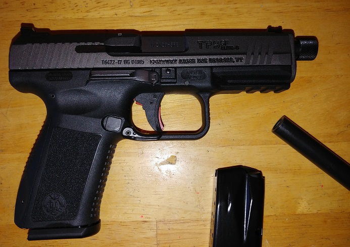 Black handgun with detached magazine and barrel on a wooden surface.
