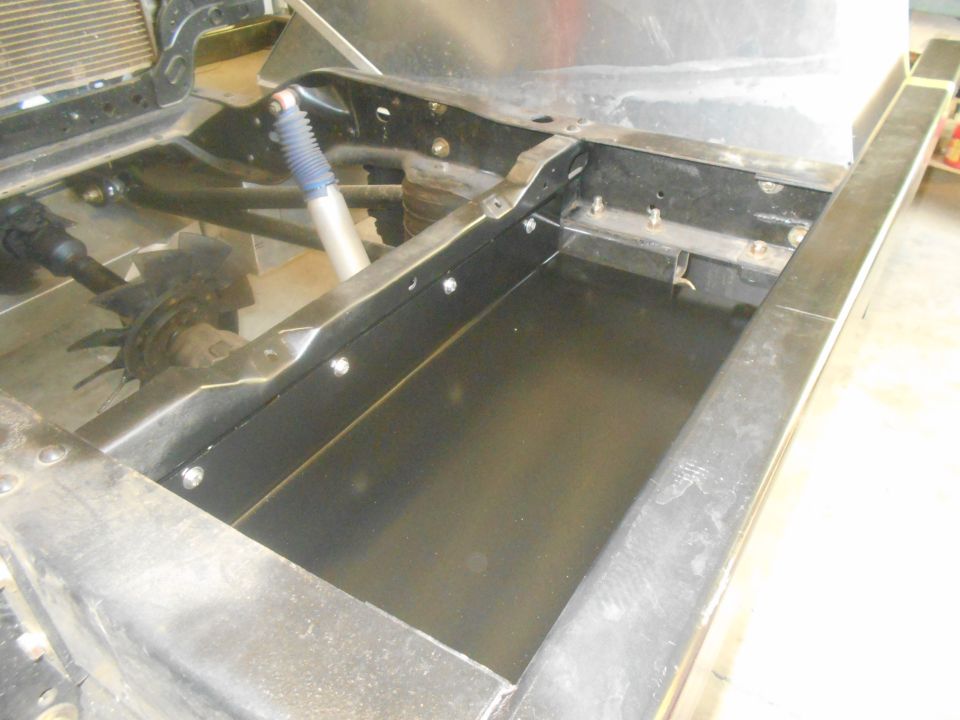 Vehicle chassis with new metal framing and black floor panel, showing shock absorber and driveshaft.