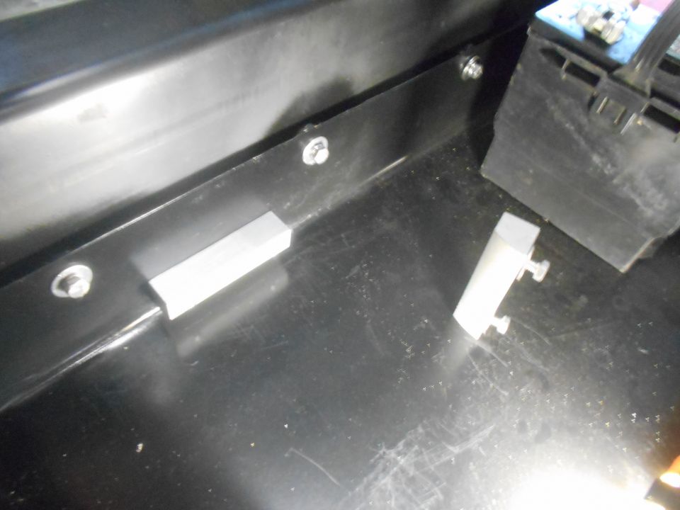 Two silver metal brackets on a black surface, with a battery in the background.