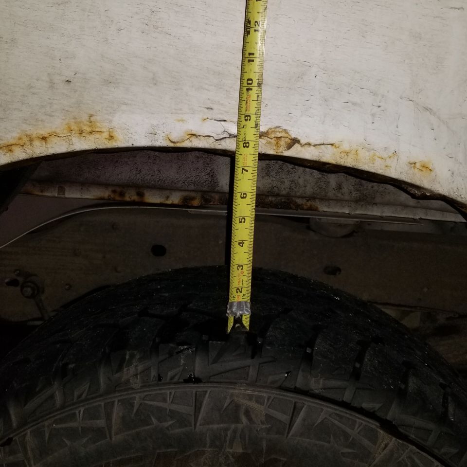 Measuring tire clearance in a rusty wheel well of a 1995 Ford Bronco.