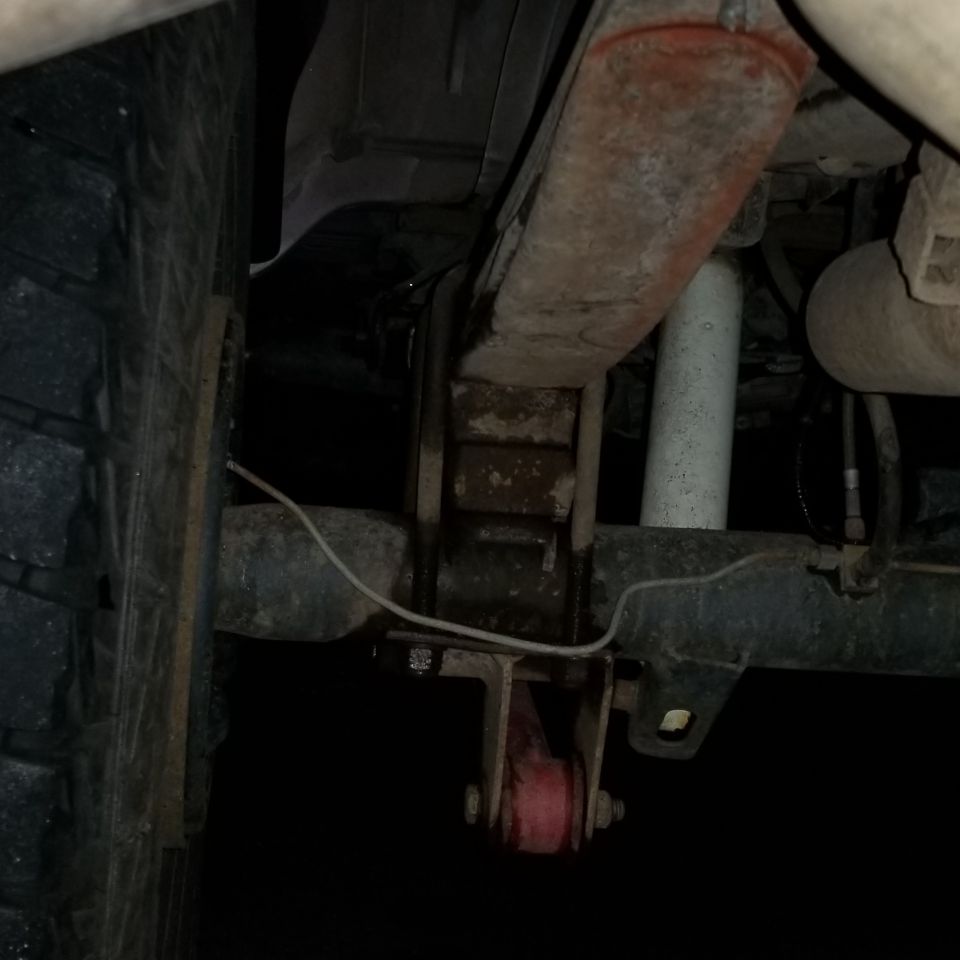Underside of a vehicle's rear suspension with leaf springs, shock, and red aftermarket part.