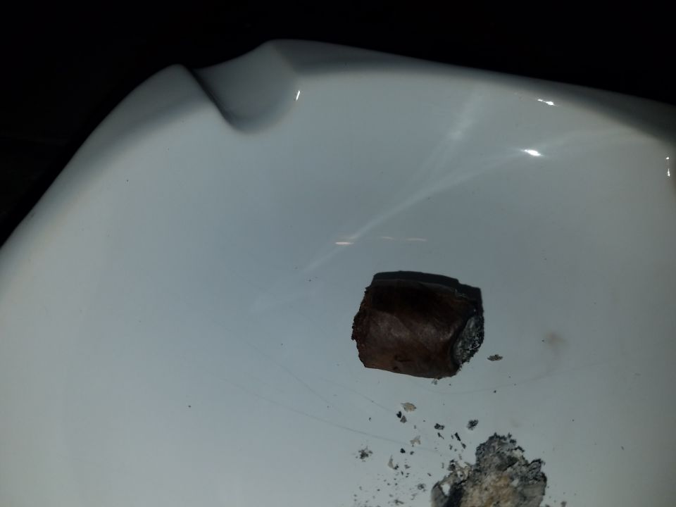 A cigar stub and ash in a white ashtray.