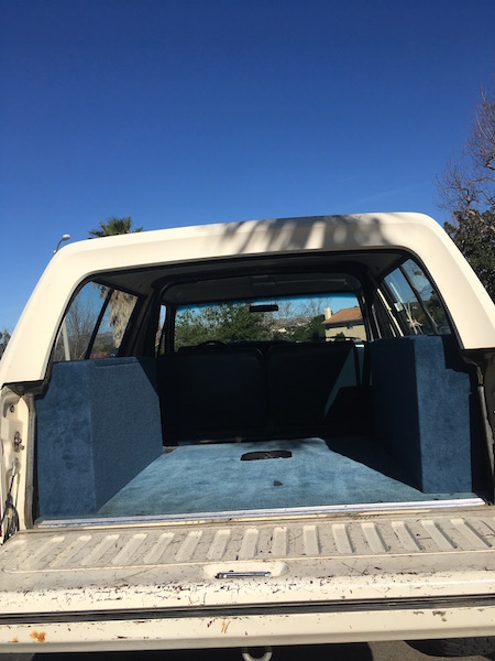 1981 Ford Bronco - The rear interior of a classic white SUV, likely a Ford Bronco, is shown with blue carpet lining the floor and side panels. The tailgate is…