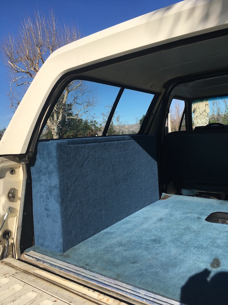 1981 Ford Bronco - The interior of a vehicle is shown, featuring blue carpeting on the floor and a custom-built blue upholstered box against the rear wall. Th…