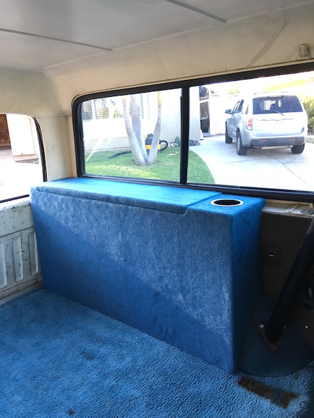 1981 Ford Bronco - The interior of a vehicle shows a custom blue carpeted storage box with a cup holder, positioned behind the front seats and against the rea…