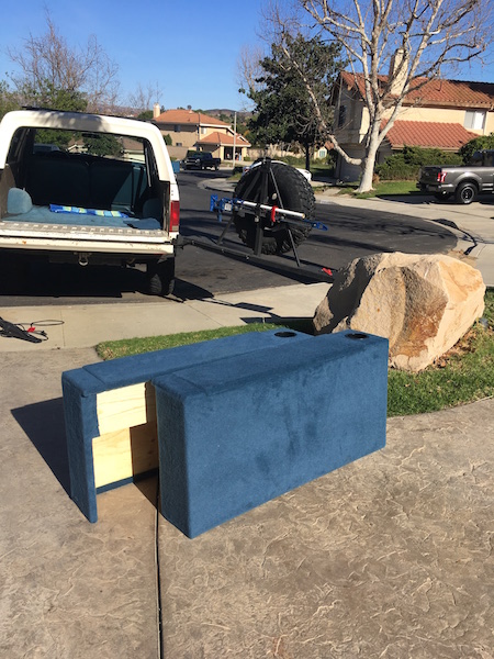 1981 Ford Bronco - A blue upholstered subwoofer box with two cup holders sits on a stamped concrete driveway in front of a white Ford Bronco with its tailgate…