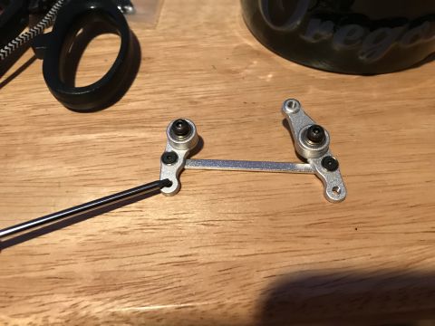 1989 Ford Bronco - A close-up shot shows a metal linkage assembly with ball bearings and screws, along with a hex wrench, on a wooden surface. A black plastic…