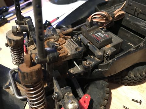 1989 Ford Bronco - Close-up view of the suspension and steering servo of an RC car, likely a 1989 Ford Bronco based on context. The components appear dusty an…