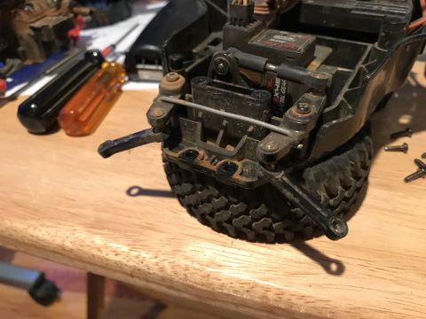 1989 Ford Bronco - A close-up view of the rear suspension and steering linkage of a remote-controlled vehicle, likely a truck, resting on a wooden surface. To…