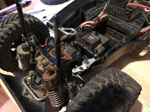 1989 Ford Bronco - Close-up view of the front suspension and steering components of a dirt-covered remote-controlled car. Visible parts include shocks, spring…