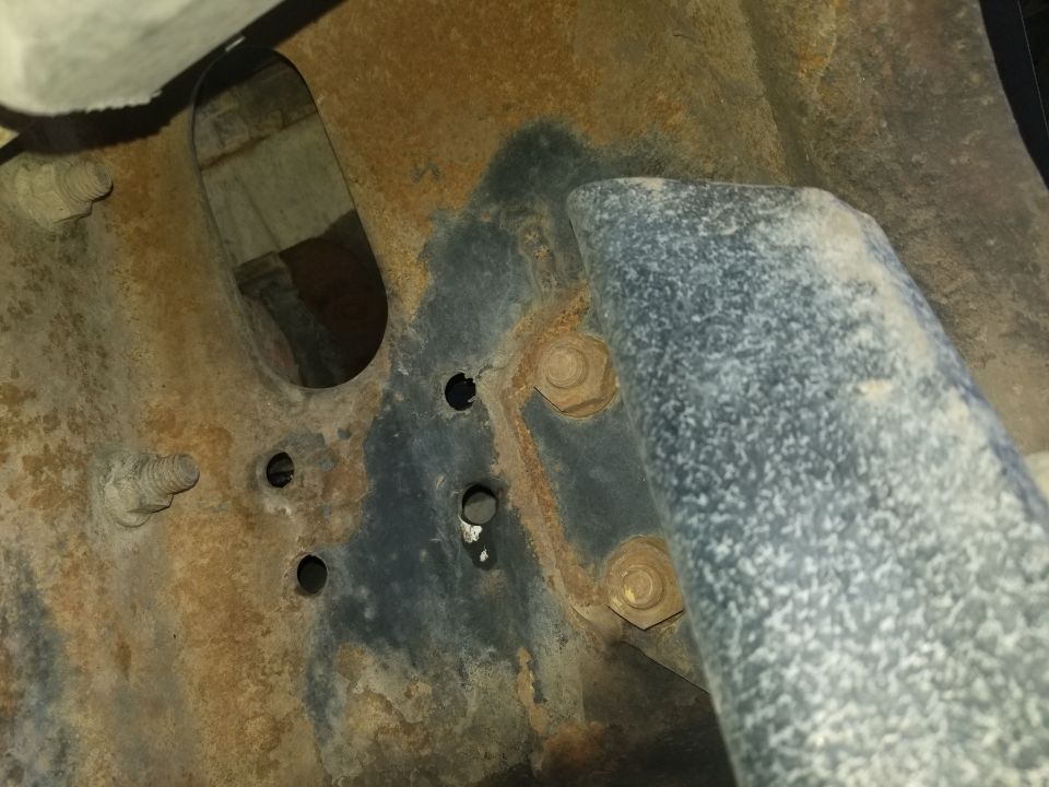 Close-up of rusty vehicle frame with bolts and a metal tube.