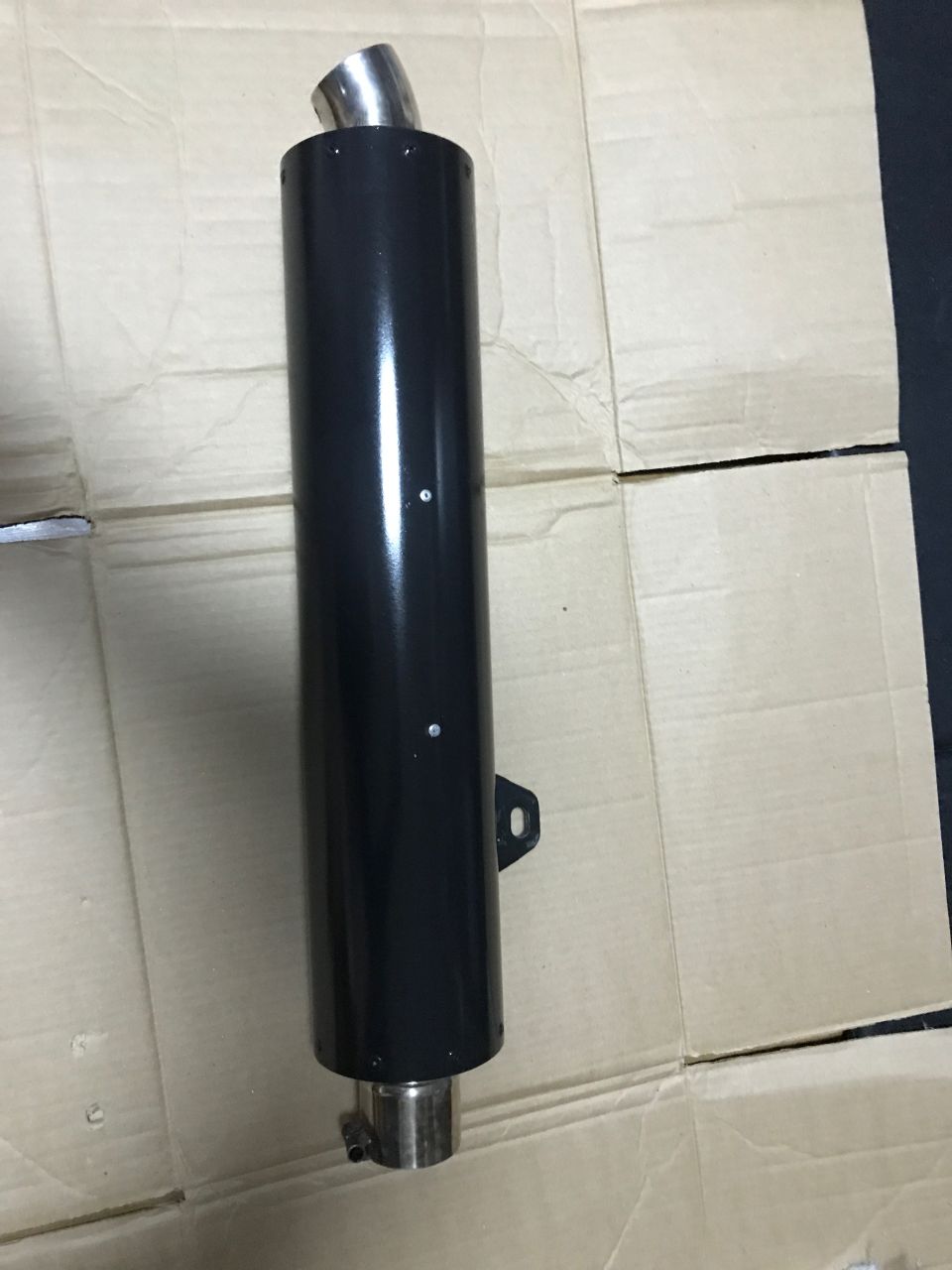 Black motorcycle exhaust muffler with silver accents on cardboard