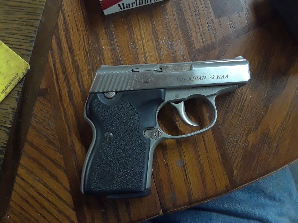 Silver and black Guardian 32 NAA handgun on a wooden table.