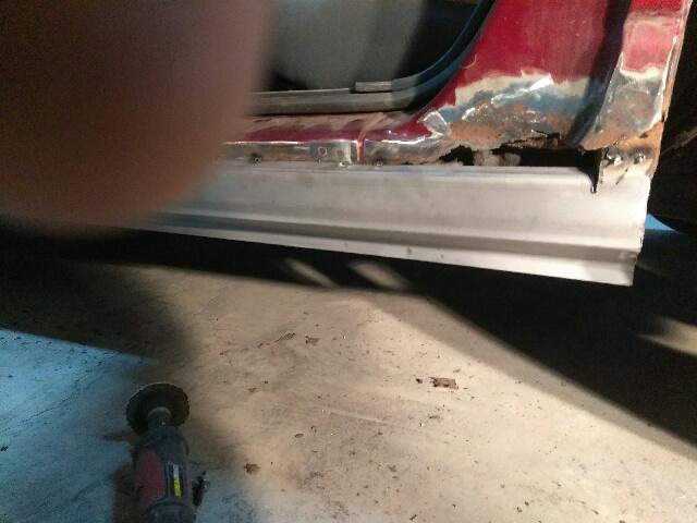 Close-up of a car's rusted rocker panel with a new silver cover installed.