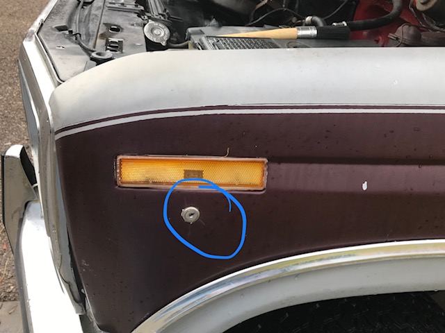 Close-up of a maroon and white car fender showing an amber turn signal and a bolt