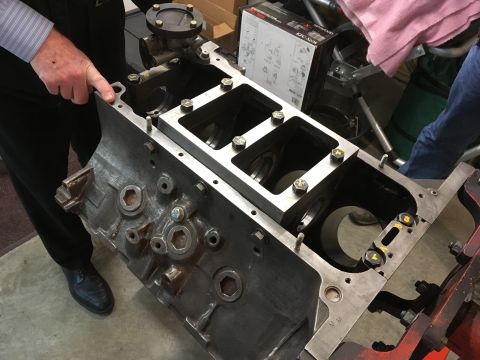 1968 Mercury Cougar - Close-up of an engine block with a person's hand pointing to a detail. A metal plate is bolted to the top of the block.