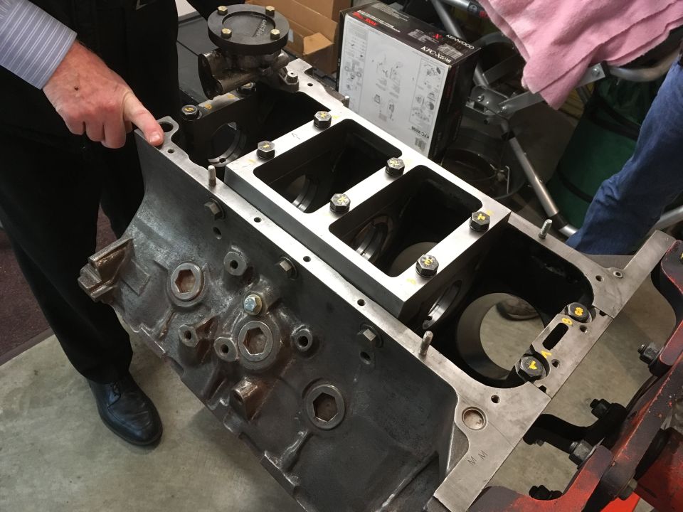 Engine block with a metal plate bolted on top, person pointing
