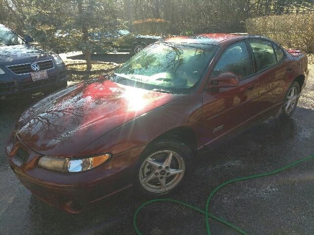 Red 2000 Pontiac Grand Prix sedan, front 3/4 view, wet surface, parked next to a dark SUV