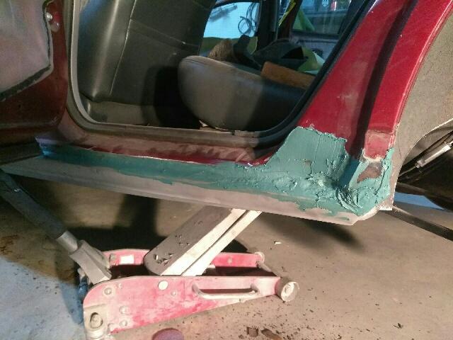 Red car door sill with green body filler and a jack underneath