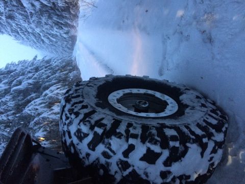 1995 Jeep YJ - A vehicle's large, snow-covered tire is the focus, set against a backdrop of a snow-covered forest and road.