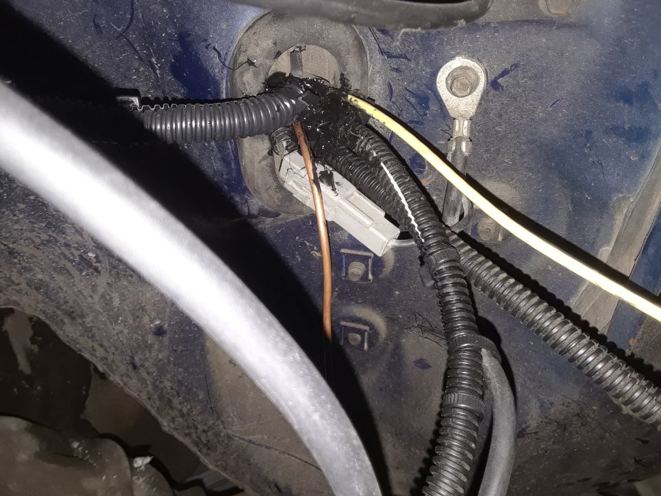 Blue vehicle body panel with a complex wiring harness, electrical tape, and a ground lug