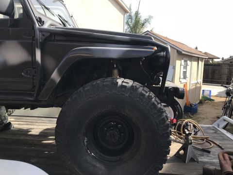 1987 Suzuki Samurai - This black off-road vehicle features large tires and a roll cage, with the front fender removed.
