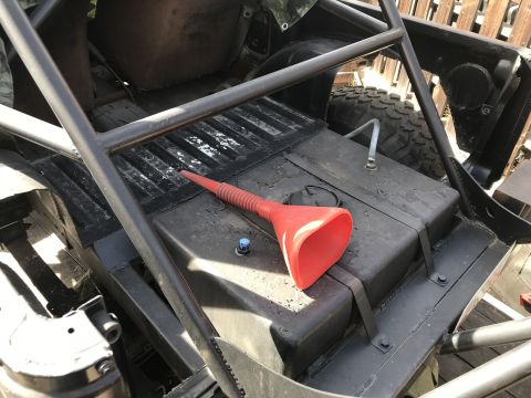 1987 Suzuki Samurai - A red funnel rests on the fuel tank of an off-road vehicle, which has a roll cage installed.