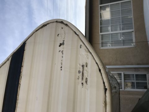 1997 Dodge 3500 - The corner of a camper shell shows significant damage, including dents and chipped paint.
